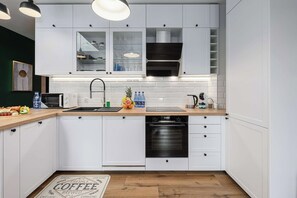 A modern kitchen with white cabinets, a stainless steel range hood, a dishwasher, and a countertop with a toaster and a fruit bowl. - Home near Piotrkowska Street (Łódź)