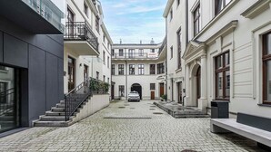 A courtyard with a paved walkway, a car parked in the center, and buildings with balconies and windows. - Home near Piotrkowska Street (Łódź)
