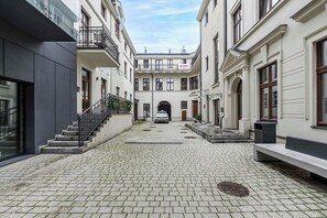 A courtyard with a paved walkway, a car parked in the center, and buildings with balconies and windows. - Home near Piotrkowska Street (Łódź)
