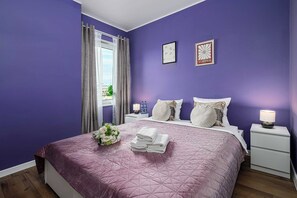 A bedroom with a bed, pillows, a nightstand, a lamp, and a window with curtains. - Home near Piotrkowska Street (Łódź)