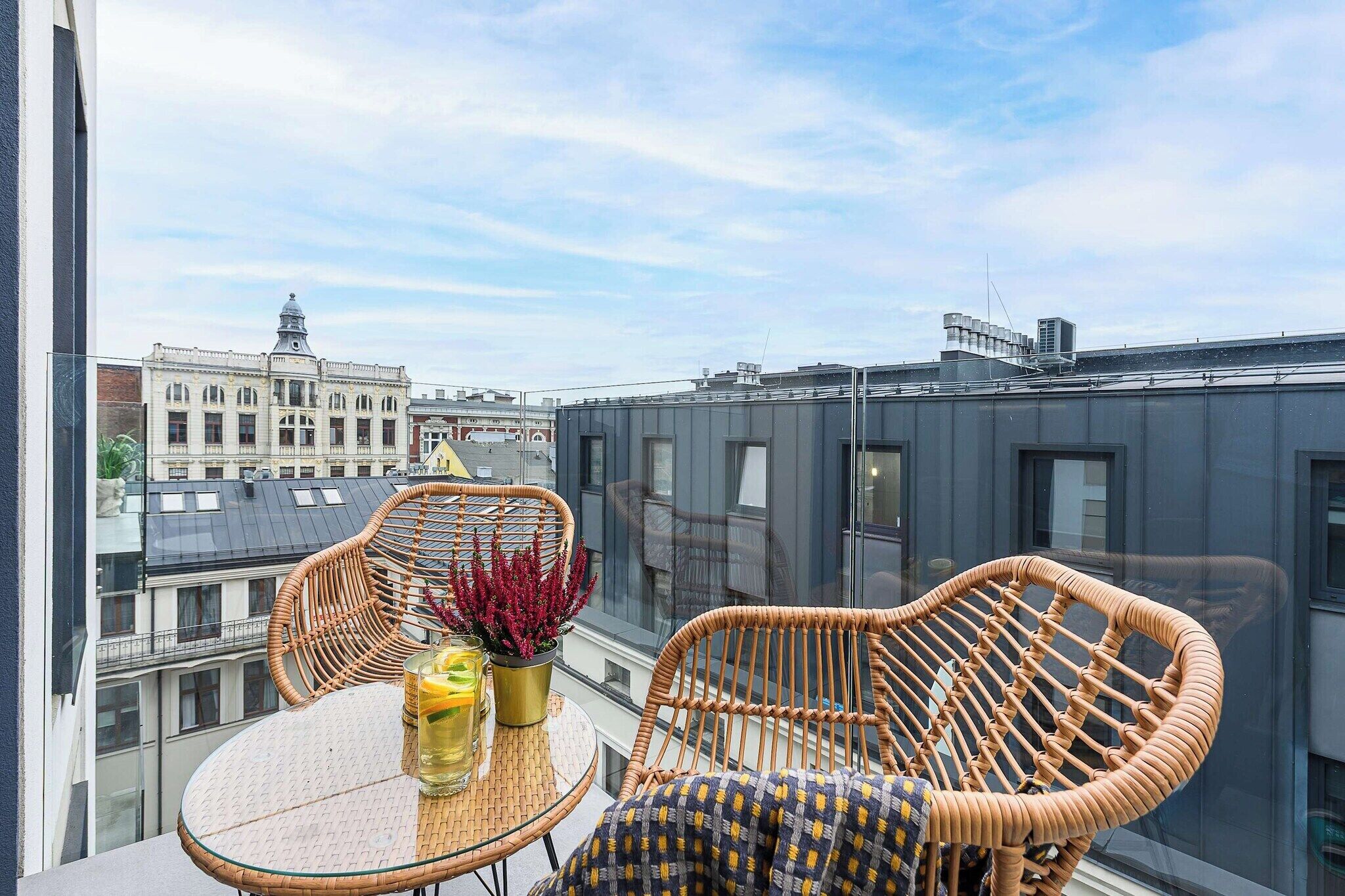 Ein Balkon mit Korbstühlen, einem Glastisch und einem Blumentopf.