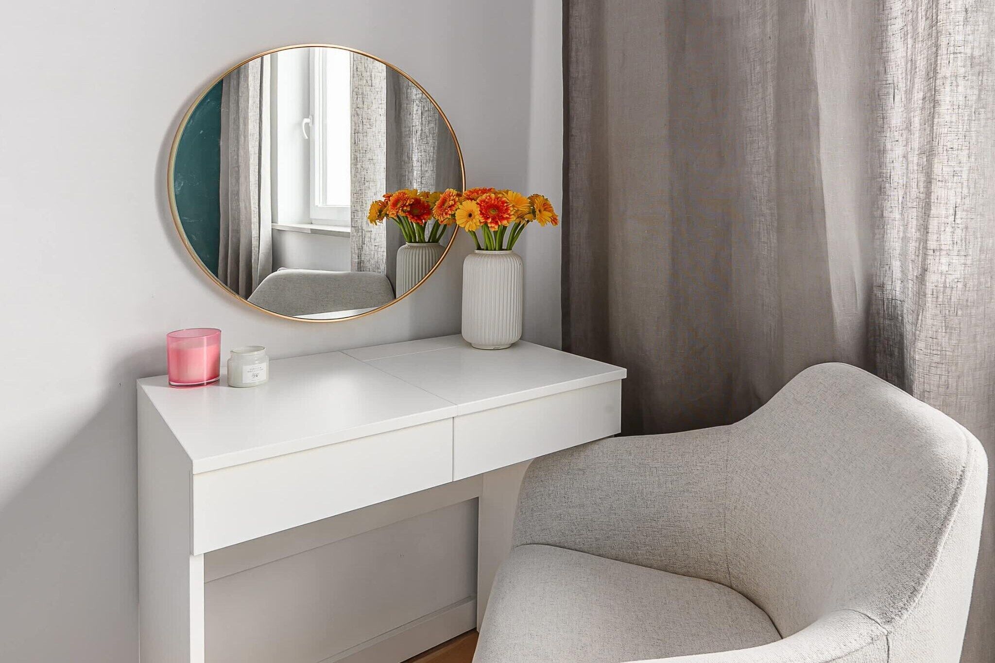 Un mobile bagno bianco con uno specchio rotondo, un vaso con fiori e una candela rosa.
