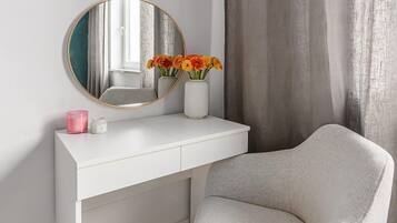A white vanity with a round mirror, a vase with flowers, and a pink candle.