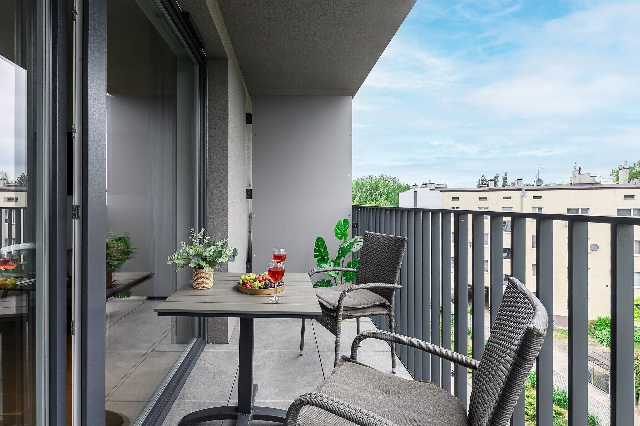 Een balkon met een tafel, stoelen, een bloempot en een glas rode wijn.