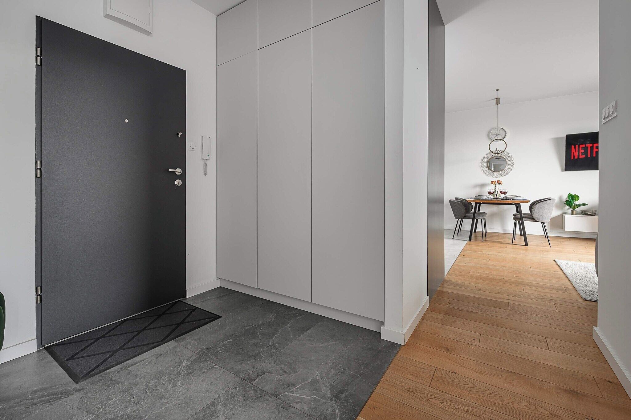 Un interno moderno con una porta scura, un armadio bianco e un'area pranzo con pavimento in legno e tavolo.