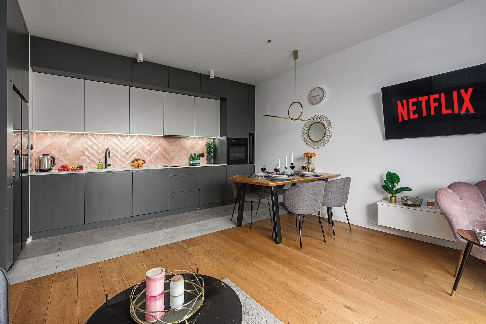 A modern kitchen with grey cabinets, a wooden dining table, and a wall-mounted Netflix sign.