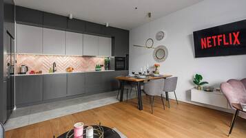 A modern kitchen with grey cabinets, a wooden dining table, and a wall-mounted Netflix sign.