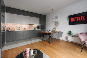A modern kitchen with grey cabinets, a wooden dining table, and a wall-mounted Netflix sign. - Air-Conditioned Apartment with Balcony in Łódź (Łódź)