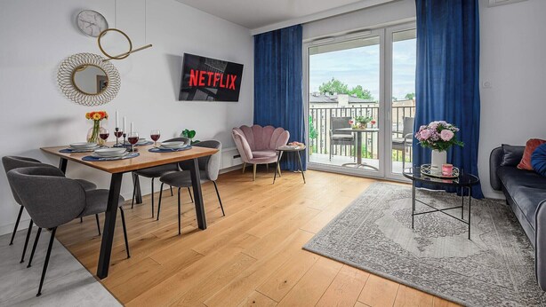 A modern living room with a dining area, a balcony with a view, and a Netflix sign on the wall. - Magnificent seafront duplex in Porspoder (Łódź)