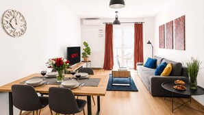 Ein modernes Wohnzimmer mit Essbereich, einer Couch, einem Couchtisch und einem Fernseher.