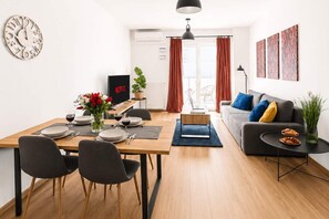 Ein modernes Wohnzimmer mit Essbereich, einer Couch, einem Couchtisch und einem Fernseher.