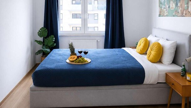 Ein modernes Schlafzimmer mit einem Bett, einem Nachttisch, einer Pflanze und einem Fenster mit Vorhängen.