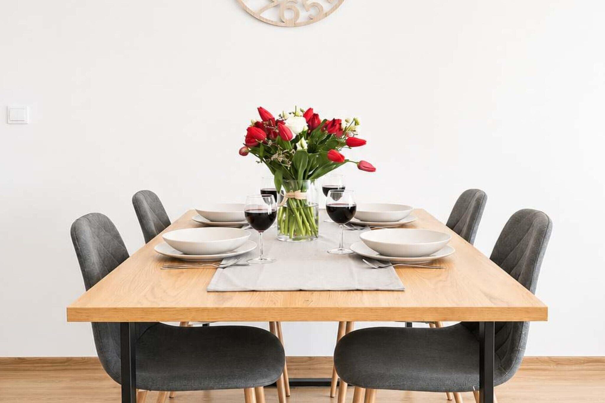 Une table à manger avec six chaises, un vase rempli de fleurs rouges et des verres à vin.