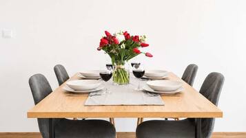 Une table à manger avec six chaises, un vase rempli de fleurs rouges et des verres à vin.