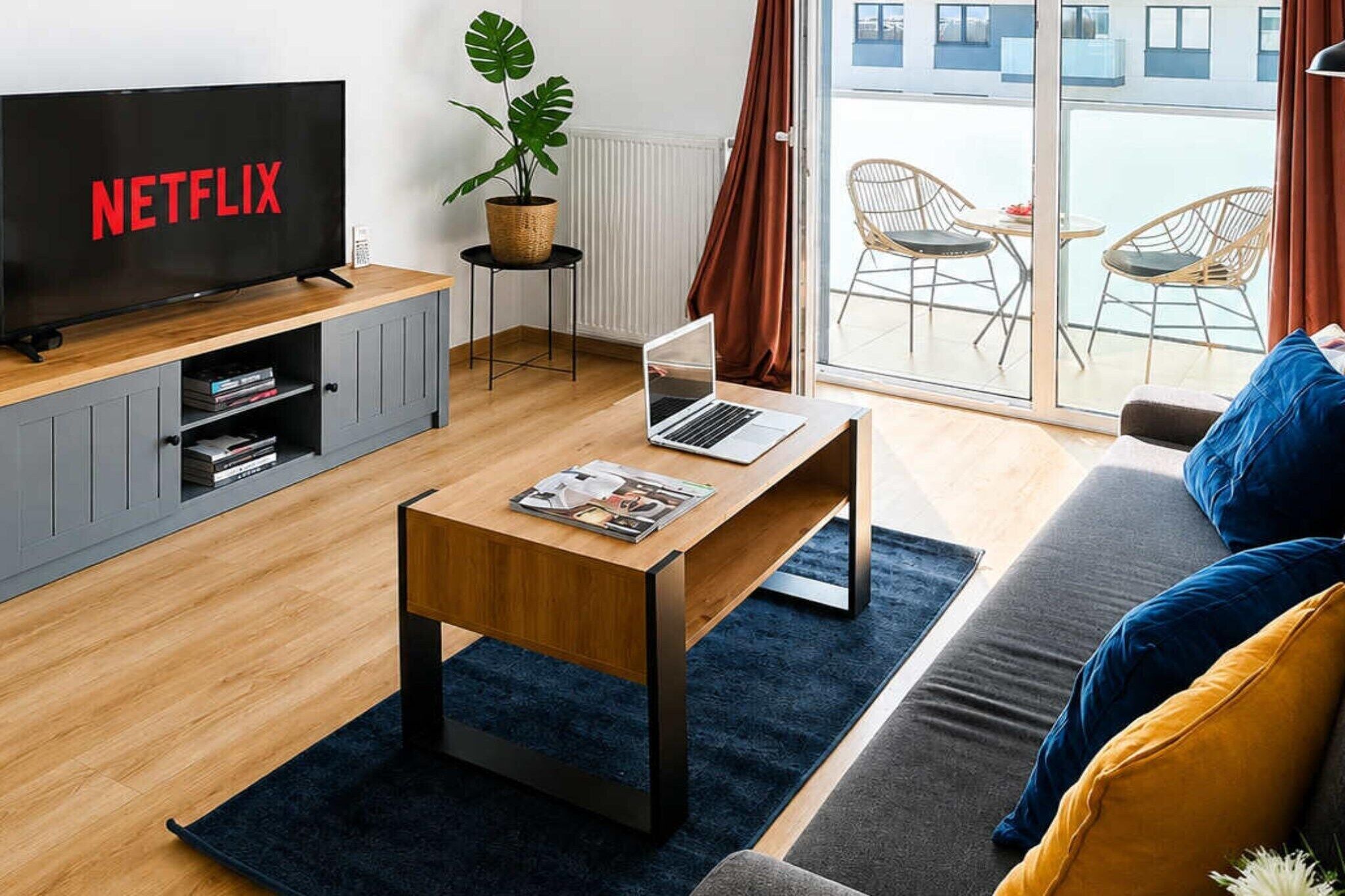 A modern living room with a television, a laptop on a coffee table, a sofa, and a view of the outdoors.