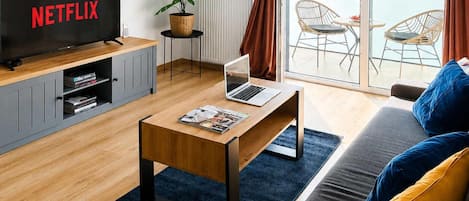 Un salon moderne avec une télévision, un ordinateur portable posé sur une table basse, un canapé et une vue sur l’extérieur.