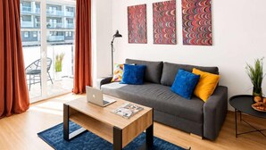 Ein modernes Wohnzimmer mit einem grauen Sofa, blauen und gelben Kissen, einem Holztisch mit einem Laptop und einem blauen Teppich.