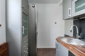 Eine kompakte Küche mit einem Edelstahl-Kühlschrank, einer Holz Arbeitsplatte und einem modernen Wasserhahn.