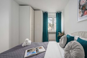 Et soveværelse med en seng, et vindue med gardiner, en radiator og et billede i ramme på væggen.