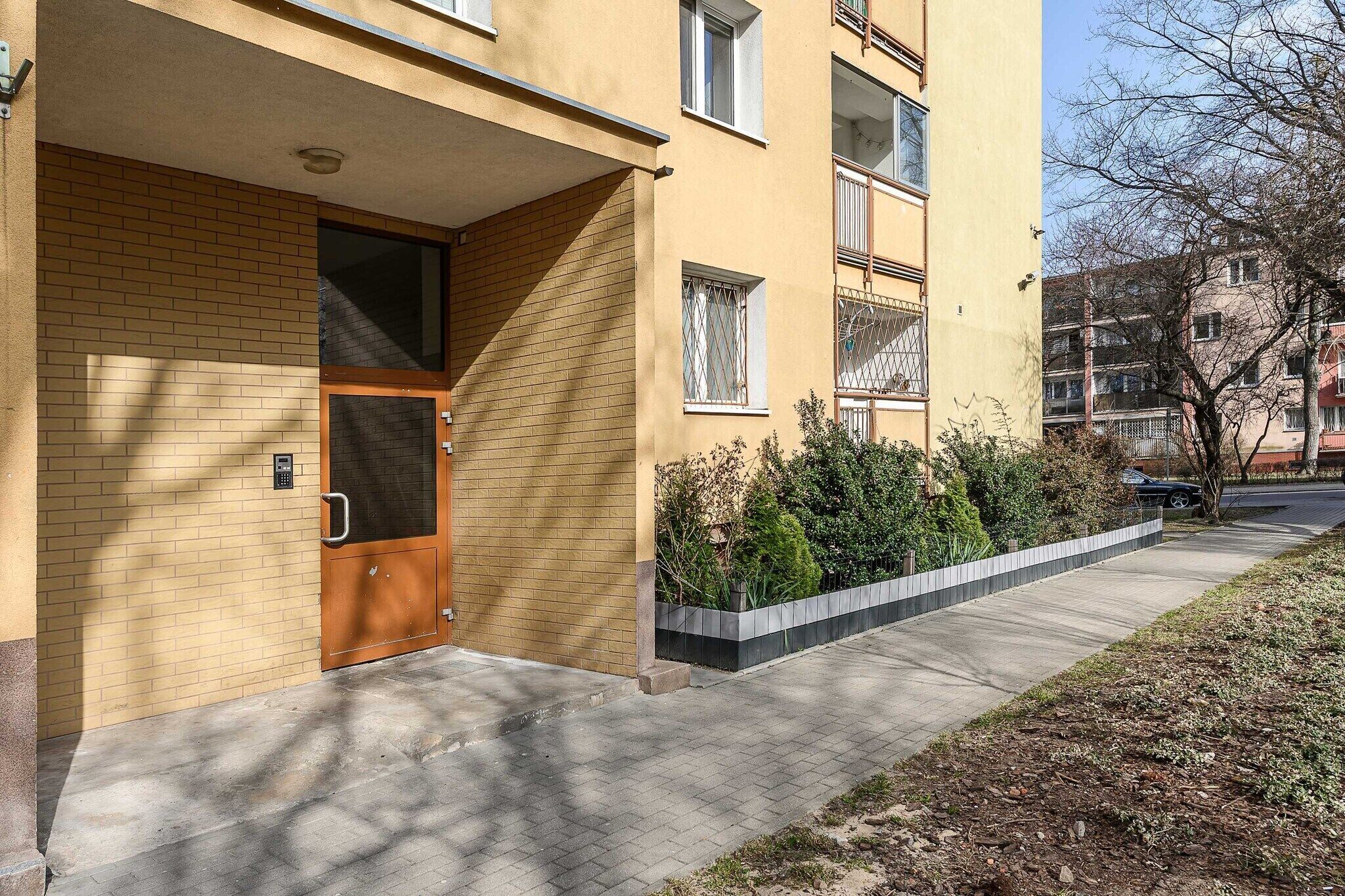 Ein Wohngebäude mit Ziegelverkleidung, einer Holztür und einem kleinen Garten mit Pflanzen.
