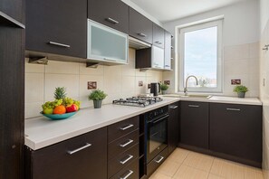 Eine moderne Küche mit dunklen Schränken, einer weißen Arbeitsplatte, einem Gasherd, einem Geschirrspüler und einem Fenster mit Ausblick.