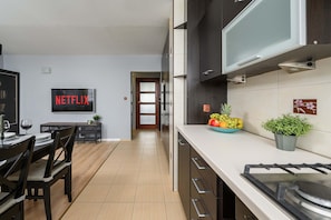 Eine moderne Küche mit Essbereich, einem an der Wand montierten Fernseher, der 'NETFLIX' zeigt, und einer Obstschale auf der Arbeitsplatte.