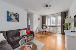 Ein modernes Wohnzimmer mit einem dunklen Sofa, einem Glastisch und einem Essbereich mit einem weißen Tisch und Stühlen.