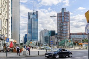 A city street with modern buildings, a pedestrian crossing, and a tram. - Stylish City Apartment for 3 Guests (Warszawa)