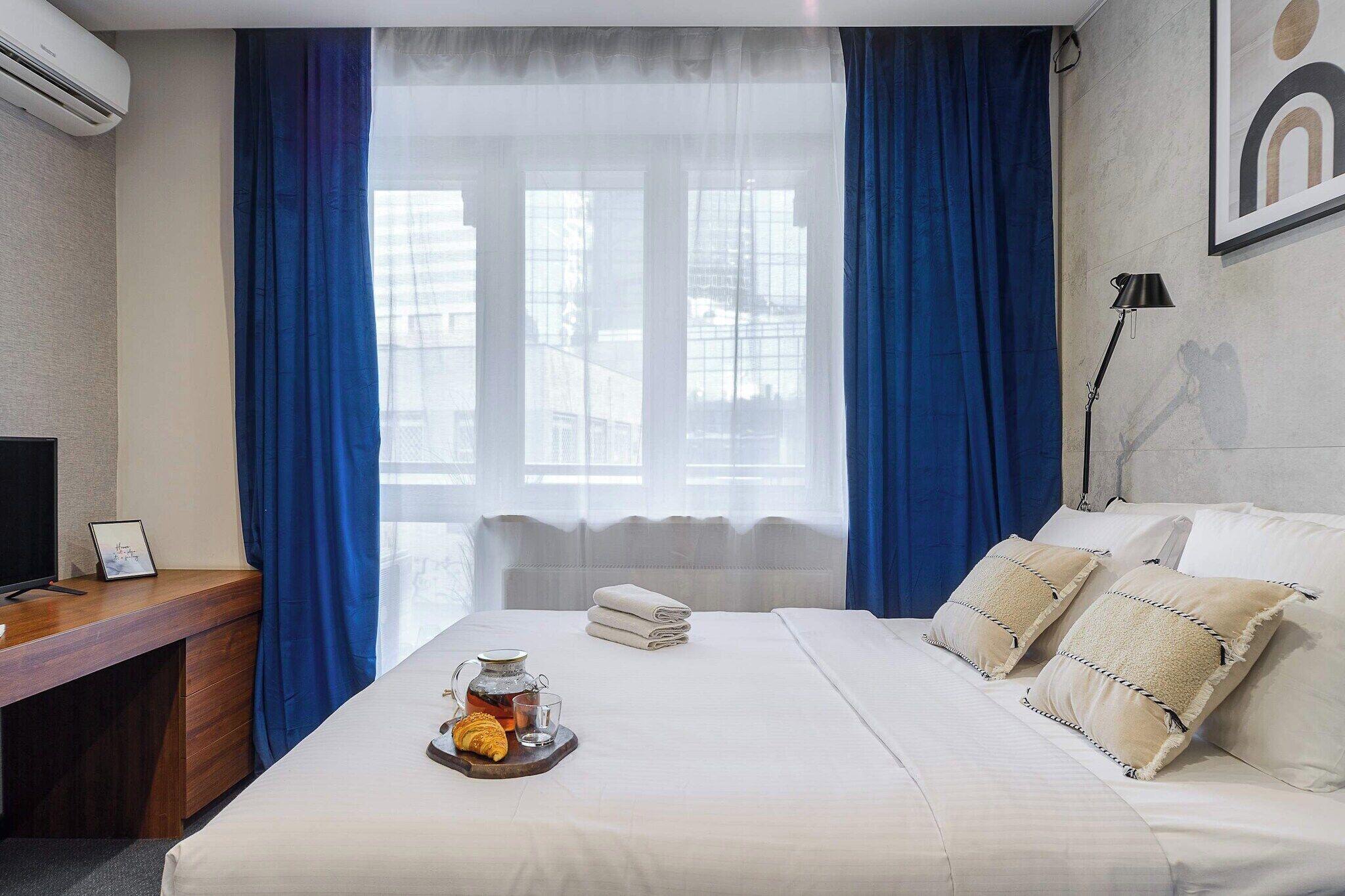 A hotel room with a bed, a desk, a lamp, and a window with curtains.