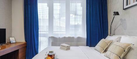 A hotel room with a bed, a desk, a lamp, and a window with curtains.