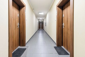 A hallway with wooden doors, a tiled floor, and a light fixture on the ceiling. - Cozy Flat near Manufaktura (Łódź)