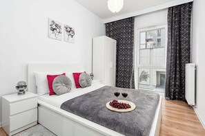 A modern bedroom with a bed, bedside tables, a radiator, and a window with curtains. - Cozy Flat near Manufaktura (Łódź)