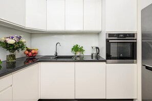 A modern kitchen with white cabinets, a black countertop, a sink, a kettle, and an oven. - Cozy Flat near Manufaktura (Łódź)
