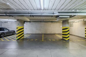 A parking garage with concrete pillars, yellow and black striped barriers, and a car parked in one of the spaces. - Cozy Flat near Manufaktura (Łódź)