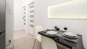 A modern kitchen with a dining table set for two, white chairs, and a countertop with a black speckled backsplash. - Cozy Flat near Manufaktura (Łódź)