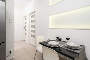A modern kitchen with a dining table set for two, white chairs, and a countertop with a black speckled backsplash. - Cozy Flat near Manufaktura (Łódź)