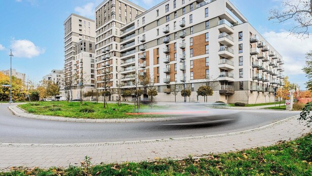 A multi-story residential building with balconies, a landscaped area with trees, and a road in the foreground. - Cozy Flat near Manufaktura (Łódź)