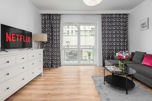 A modern living room with a flat-screen TV, a sofa, a coffee table, and a decorative vase. - Cozy Flat near Manufaktura (Łódź)
