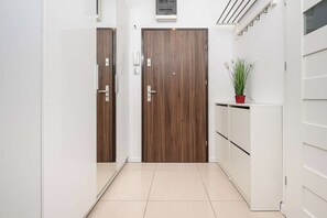 A hallway with two wooden doors, a white cabinet, and a potted plant. - Cozy Flat near Manufaktura (Łódź)