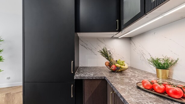 Una cocina moderna con armarios oscuros, encimera de mármol y un frutero.