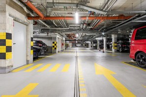 Eine mehrstöckige Tiefgarage mit deutlichen Richtpfeilen auf dem Boden, zahlreichen Stellplätzen und einem roten Fahrzeug auf der rechten Seite.