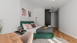 Un dormitorio moderno con una cama tapizada de verde, una mesita de noche, una lámpara y una alfombra gris.