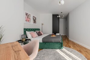Ein modernes Schlafzimmer mit einem grün gepolsterten Bett, einem Nachttisch, einer Lampe und einem grauen Teppich.