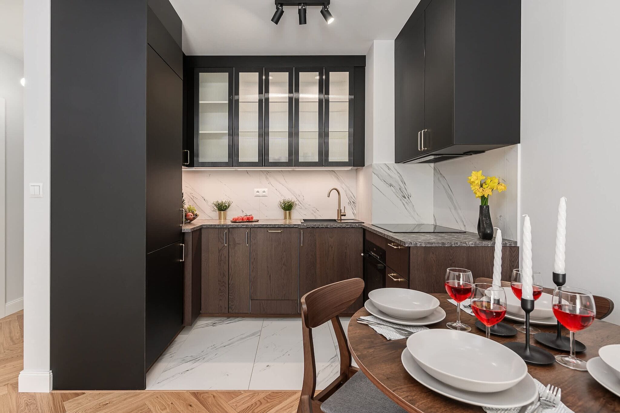 A modern kitchen with dark cabinetry, a marble countertop, and a dining area set for a meal.