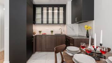 A modern kitchen with dark cabinetry, a marble countertop, and a dining area set for a meal.