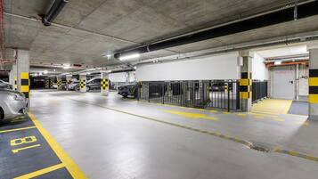 A multi-level parking garage with concrete pillars, yellow and black striped barriers, and marked parking spaces.