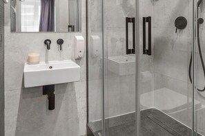 A modern bathroom with a white sink, a mirror, and a glass-enclosed shower area. - Stylish Urban Apartment for 3 (Warszawa)