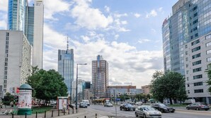 A city street with modern buildings, a tram, and cars. - Stylish Urban Apartment for 3 (Warszawa)