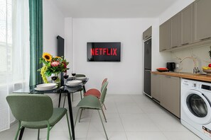A modern kitchen with a built-in washer, a dining area with a table set for two, and a wall-mounted TV displaying 'NETFLIX'. - Warsaw Apartment for 6 with Parking (Warszawa 2)