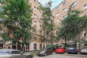 Ein mehrgeschossiges Wohngebäude mit parkenden Autos und Bäumen davor.